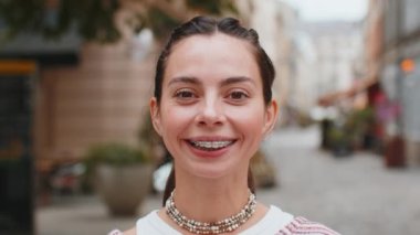 Dişlerini diş telleriyle gösteren, eğlenen, gülen ve şehir caddesinde kameraya bakan mutlu beyaz kadın portresi. Dişli gülümseme. Güzel kız dişçilikten memnun.