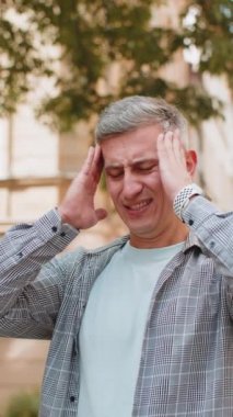 Kafkasyalı adamın baş ağrısı problemini tedavi etmek için tapınakları ovmasından memnun değilim. Olgun erkek turist suratını buruşturuyor, şehirde acı çekiyor. Dikey.