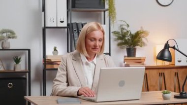 İç işlerinde masa başında otururken laptoptan harika haberler okuyan mutlu beyaz kadın başarısını kutluyor. Gülümseyen iş kadını güzel bir tebliğden memnun, evet işareti gösteriyor..