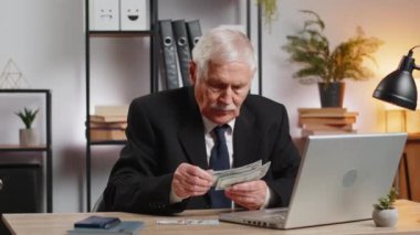 Diz üstü bilgisayarda çalışan zengin bir büyükbaba işadamı nakit para sayıyor, iş yerindeki gelir gelirlerini hesaplıyor. Profesyonel serbest meslek sahibi. İş adamları. İstihdam mesleği