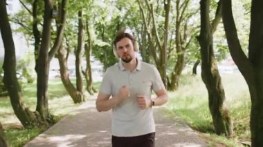 Sporcu spor koşucusu maraton koşusu yapıyor, kulaklıkla müzik dinliyor. Sabah parkta kardiyo çalışması var. Sağlıklı yaşam tarzını seven mutlu genç bir adam. Aktif sporcu koşucu.