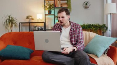Evdeki kanepede oturup dizüstü bilgisayar kullanan sinirli ve stresli genç bir adam. Ekose gömlekli beyaz adam kötü piyango oyununu kaybetmeye tepki veriyor. Oturma odasında netbook 'ta haberler var..