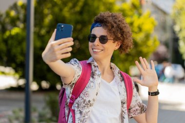 Mutlu genç blog yazarı akıllı telefondan selfie çekiyor, abonelerle çevrimiçi video görüşmesi yapıyor, sosyal medya vlog 'u için hikayeler kaydediyor. Şehir merkezinde yürüyen adam..