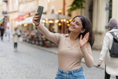 Hintli genç blog yazarı akıllı telefondan selfie çekiyor, abonelerle çevrimiçi video görüşmesi yapıyor, sosyal medya vlog 'u için hikayeler kaydediyor. Şehir caddesinde yürüyen İspanyol kız