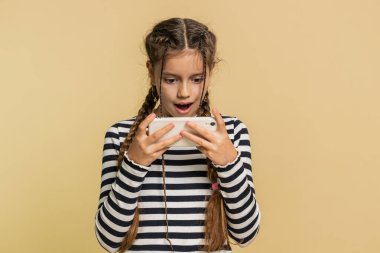 Heyecanlı genç kız çocuk oyuncu zaferi heyecanlı bir şekilde kutluyor yarış simülatörü ya da akıllı telefondan video oyunları oynuyor. Bej arka planda izole edilmiş genç çocuklar