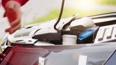 Servis çalışanı araba kaputunun motor dairesine kırmızı cam silecekleri temizleyen cam silecekleri teneke kutudan dolduruyor. Ön cam suyu ön cam yıkama tankına karışıyor.