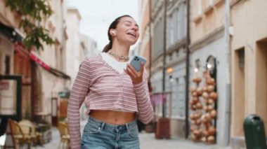 Kablosuz kulaklıklı mutlu, gevşemiş yetişkin kız dışarıda dans eden enerjik disko rock n roll müziği dinliyor. Beyaz bir kadın yaz caddesinde yürüyor..