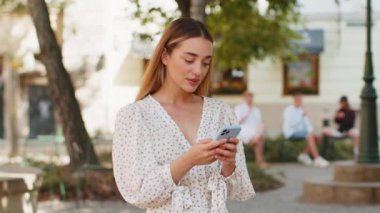 Akıllı telefon kullanarak gülümseyen genç bir kadın. Kısa mesajlar yazarak interneti tarıyor, işi bitiriyor, dışarıdaki kameralara bakıyor. Şehir caddesinde giyinmiş bir kız turist. Kasaba yaşam tarzları.