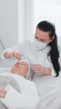 Kozmetik uzmanı, özel nemlendirici asit kokteyli uyguluyor. Kadının gözlerinin etrafına yüz derisi soyuluyor. Güzellik salonunda yüz bakımı yaşlanmayı önleyen kozmetik tedavi prosedürü. Kırışıklıklar gideriliyor