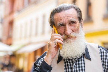 Yetişkin turist kıdemli adam arkadaşlarıyla uzaktan iletişim kuruyor. Yaşlı büyükbaba telefonda konuşuyor. Habersiz dedikodu. Şehir caddesinde yürüyor.