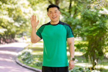 Merhaba, hoş geldiniz. Atletik zinde koşan yetişkin bir adam konuksever bir gülümsemeyle avuç içi selamlaşmayla selam veriyor. Japon genç erkek antrenmanı sabah parkta yapılıyor. Aktif sağlıklı sporcu.