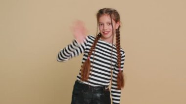 10 yaşındaki tatlı kız kameraya gülümseyip el sallayarak merhaba ya da hoşça kal diyor. Misafirperver bir ifadeyle karşılıyor. Bej arka planda izole edilmiş reşit olmayan çocuk.