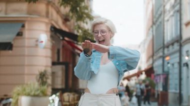 Neşeli, zengin, mutlu bir kadın el hareketi yaparak para harcıyor, daha fazla bahşiş kazanıyor, büyük kar ediyor, piyango kazanıyor, paylaşıyor, dışarıda kutluyor. Genç sarışın bayan gezgin şehir caddesinde duruyor..