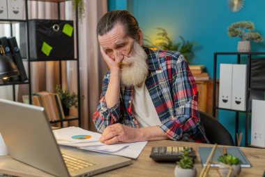 Yorgun ve yorgun kıdemli serbest çalışan evrak işlerini, muhasebe ödemelerini ve ofis masasındaki aylık harcamaları analiz ediyor. Büyükbabanın uzaktan kumandalı bir işte çalışmasına üzüldüm..