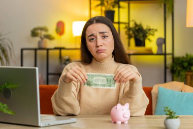 Zavallı Kafkas genç kadın, yetersiz miktarda para, kumbarası ve bir dolar banknotu var. Finansal kriz. İflas. Yoksulluk, yoksulluk. Masada ev ofisinde oturan kadın.