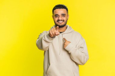 Seni seçiyorum. Hintli gülümseyen adam kamerayı işaret ediyor ve neşeli bir ifadeyle bakıyor, kazanan seçimi yapıyor, yön gösteriyor. Sarı stüdyo arka planında izole Arap genç adam