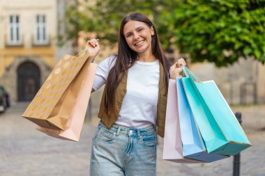 Alışveriş merkezinde alışveriş yaptıktan sonra açık havada hediyelerle dolu poşetlerle gülümseyen esmer, genç bir kadın tüketici. Şehir caddesinde günlük kıyafetlerle gezen turist kız. Kasaba yaşam tarzları.