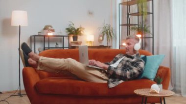 Kablosuz kulaklıklı, evinde kanepeye uzanmış, dizüstü bilgisayar ağı üzerinde çalışırken disko müziği dinlemeyi seçen mutlu, rahat, beyaz bir genç adam. Erkekler hafta sonları eğleniyor.