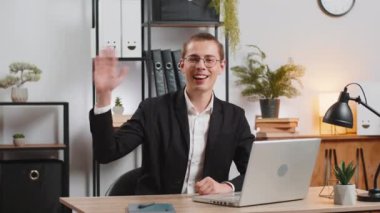 Portre görüntüsü, gülümseyen genç işadamının iki elini sallamasının portre görüntüsü. İnternetteki konferans videosundaki interinterinterinterinterinterinterinterinterinterinterinterinterinterinterinterinterinterlocutor 'a merhaba imzası atıyor. Takım elbiseli adam..