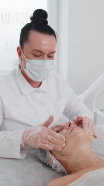 Kozmetik uzmanı özel nemlendirici krem uyguluyor, güzel beyaz bir kadının yüzünü ovuyor, soyuyordu. Güzellik salonunda yüz bakımı yaşlanmayı önleyen kozmetik masaj prosedürü. Güzellik tedavisi