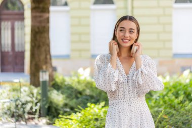Neşeli, neşeli, yetişkin bir kız, açık havada dans eden ve favori disko rock n roll müziğini dinleyen. Kablosuz kulaklıklarını çıkartıp yan tarafa bakan kadın sokakta gülümsüyor..