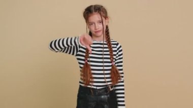 Hoşlanmamak. Üzgün, çocukluk çağındaki kız çocuğu işaret dilini göstererek hoşnutsuzluğunu, hoşnutsuzluğunu ve evde kötü çalışmasını ifade ediyor. Bej renkli stüdyo arka planında tatsız çocuklar.