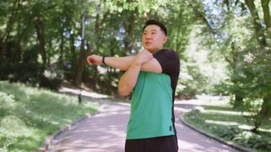 Japon sporcu sporcu, saglikli bir adam, parkta, orman dogasinda, ellerini uzatiyor, kollarini geriyor, sabah sporu, egzersiz, saglik hizmetleri. Sporcu yaşam tarzları.