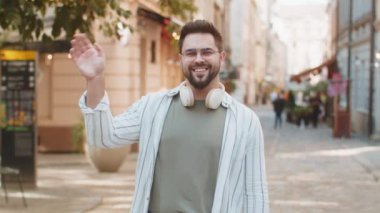Neşeli genç turist, kameraya gülümseyen, el sallayan, el sallayan davetkar, merhaba, hoşça kal, selamlayan, misafirperver bir yüz ifadesiyle karşılayan. Şehir merkezindeki adam..