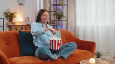 Heyecanlı genç bir kadın turuncu koltukta oturup patlamış mısır yiyor ve evde ilginç TV dizileri, spor oyunları, filmler, çevrimiçi sosyal medya filmleri izliyor. Kız ev eğlencesinden hoşlanıyor.