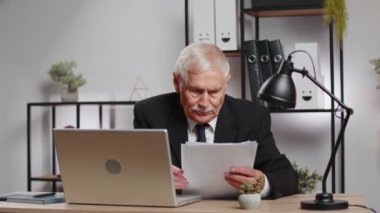 Finansal grafik belgeleriyle çalışan kıdemli serbest muhasebeci. Haritalar için vergileri ve ofis masasındaki raporları hesaplıyor. İş adamı büyükbaba dizüstü bilgisayar planlama masrafları bütçesinde çalışıyor.