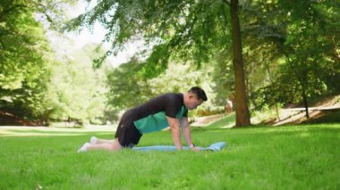 Mutlu Asyalı Japon adam parkta egzersiz yapıyor, yoga yapıyor, spor antrenmanlarını minder üzerinde yapıyor. Aktif Çinli sporcu güneşli yaz gününde sağlıklı yaşam tarzının tadını çıkarıyor. Genç adam egzersiz yapıyor..