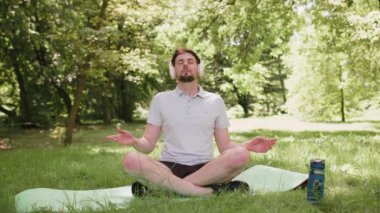 Lotus pozisyonunda oturan genç adam yaz günü şehir parkında dinleniyor. Sportif kaygısız adam yoga meditasyonu yapıyor, pozitif enerji alıyor, sağlıklı yaşam tarzı var. Aktif rahatla sporcu.