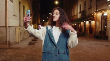Mutlu ergen çocuk blogcu akıllı telefondan selfie çekiyor, sosyal medya vlog 'u için abonelerle çevrimiçi video görüşmesi yapıyor. Gece şehir caddesinde dikilen genç kız.