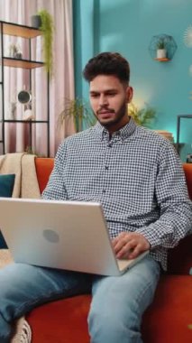 Laptop bilgisayar kullanan Hintli genç adam, iyi haber mesajı alıyor. Aniden kazanılan piyango galibiyetini kutluyor. Evdeki kanepede online alışveriş oyunu oynuyor.