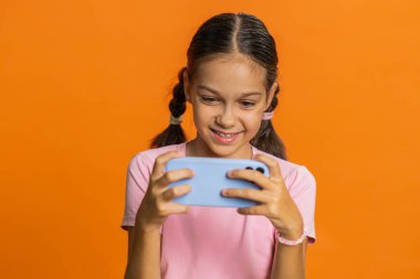 Heyecanlı genç kız çocuk oyuncu zaferi heyecanlı bir şekilde kutluyor yarış simülatörü oynuyor, akıllı telefondan video oyunları oynuyor. Turuncu arka planda izole edilmiş genç çocuklar