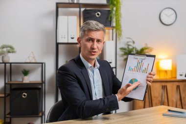 Merkez büro masasında çalışan beyaz iş adamının POV 'u grafik analizleri gösteriyor ve çalışanla çevrimiçi iletişim videosu hakkında konuşuyor. Freelancer destek servisi kameraya bakıyor..