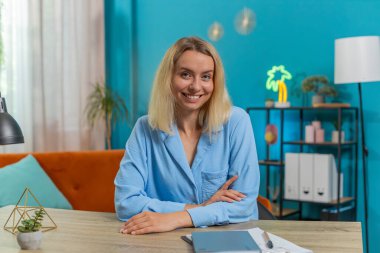 Ofis masasında kameraya bakan gülümseyen sarışın, beyaz iş kadınının portresi. Oturma odasındaki masada oturan serbest çalışan bir bayan. Mavi elbiseli kız..