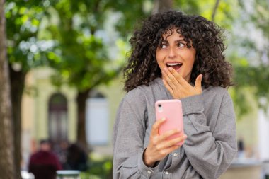 Aman Tanrım. Vay canına. Heyecanlı mutlu beyaz kadın akıllı telefon kullanarak dışarıda piyango kumarhanesi zaferini kutluyor. Şehir caddesindeki bayan kız. Güneşli park