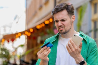Kafkasyalı bir adam internet üzerinden alışveriş yapmaya çalışırken kredi kartı bloke edilmiş cep telefonuyla şok olmuş. Sokaktaki kızgın erkek turist bankanın reddetme sorununu satın alıyor ödeme eksikliği para dengesi