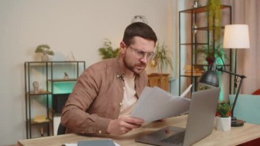 Stresli genç işadamı ödenmemiş banka borçlarına bakıyor, evrak işleriyle uğraşıyor, bütçe planlaması ipotek ödemelerini hesaplıyor. Serbest çalışan adam ofis masasına kağıt para atıyor.