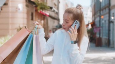 Mutlu beyaz kadın turist portresi, gülümseyen gülen şehir caddesinde elinde paketlerle durup telefonla konuşarak arkadaşına indirimlerden, alışveriş konseptinden bahsediyor..