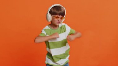 Mutlu gülümseyen, kulaklıklı, müzik dinleyen, dans eden, eğlenen, el kol hareketi yapan, komik hareketler yapan çocuk. Turuncu arka plandaki çocuk