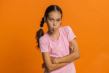 Neşeli, komik, genç liseli kız kameraya dil gösteriyor, dalga geçiyor, şakalaşıyor, zorbalıkla dalga geçiyor. Turuncu arka planda 10 yaşında çocuk.