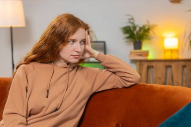 Evdeki oturma odasındaki kanepede oturan, gündelik elbiseli, yalnız, yalnız, genç bir kadın sorunları düşünüyor. Sıkılmış kadın kız, daireye bakarken kendini kötü hissediyor..