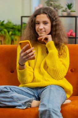Genç kız çocuk akıllı telefon sosyal medya uygulamaları üzerinden rahatlama filmi izlerken mesajlarını paylaşıyor. Beyaz çocuk evde, oturma odasındaki koltukta cep telefonu kullanıyor. Dikey