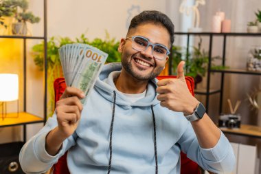 Başarılı zengin iş adamı Hindu adam yüksek karla para sayıyor, piyango kazancını kutluyor, gelir kazancını tatmin ediyor, evde dolarları elinde tutuyor.