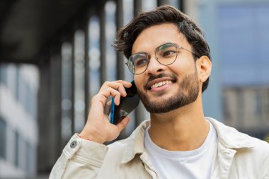 Uzaktan iletişim kuran gülümseyen Hintli adam dışarıda akıllı telefonla konuşuyor. Arap Hindu adam şehir merkezinde beklenmedik bir şekilde iyi haber dedikodusu yapıyor. İş adamları
