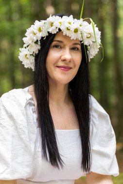 Gülümseyen orta yaşlı beyaz kadın portresi vahşi papatya çiçeklerinin çiçekleri içinde kameraya bakıyor, dinleniyor, rahatlıyor dışarıda tatmin oluyor. Forest Park 'ın arka planında sağlıklı bir bayan