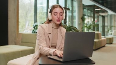 Happy, modern ofis lobisinde dizüstü bilgisayarda çalışırken, kablosuz kulaklıklı, dans eden, rahatlatıcı müzik dinleyen, neşeli, Kafkasyalı genç iş kadını. Otel odasında oturan bayan.