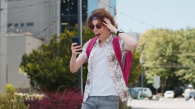 Kafkasyalı genç adam cep telefonuyla kutlama yapıyor iyi haber kazan, piyango büyük ikramiyesi kazan, açık havada internetten bağış yap. Şehir caddesinde sırt çantalı mutlu bir turist. Kasaba yaşam tarzları